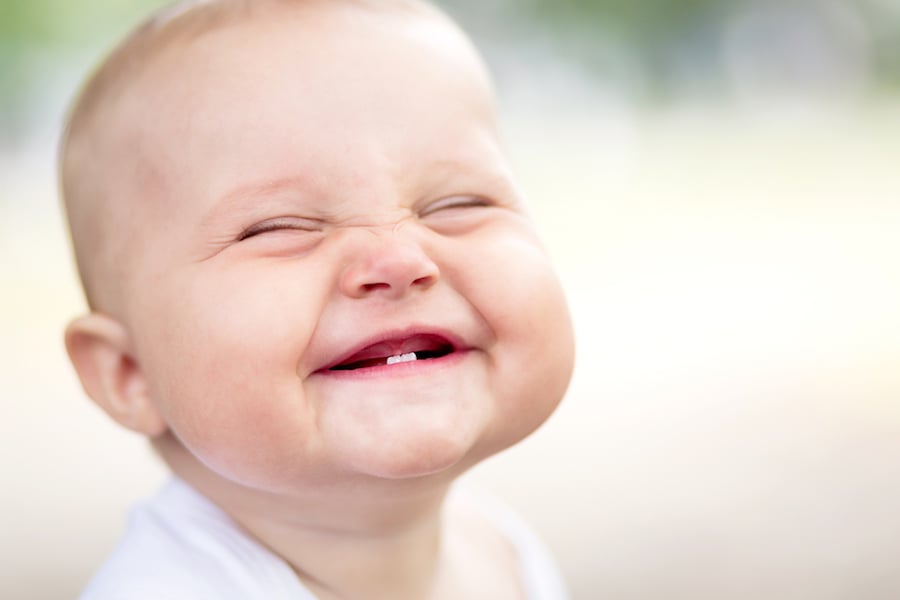 Grinning baby with two teeth scrunching up face