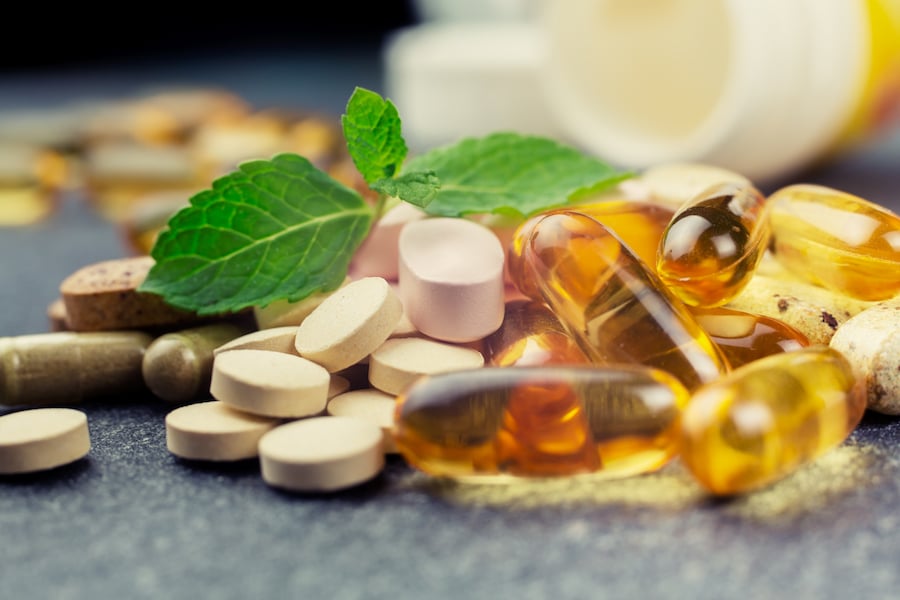 Pile of various pills with a sprig of leaves on top, signifying natural remedies