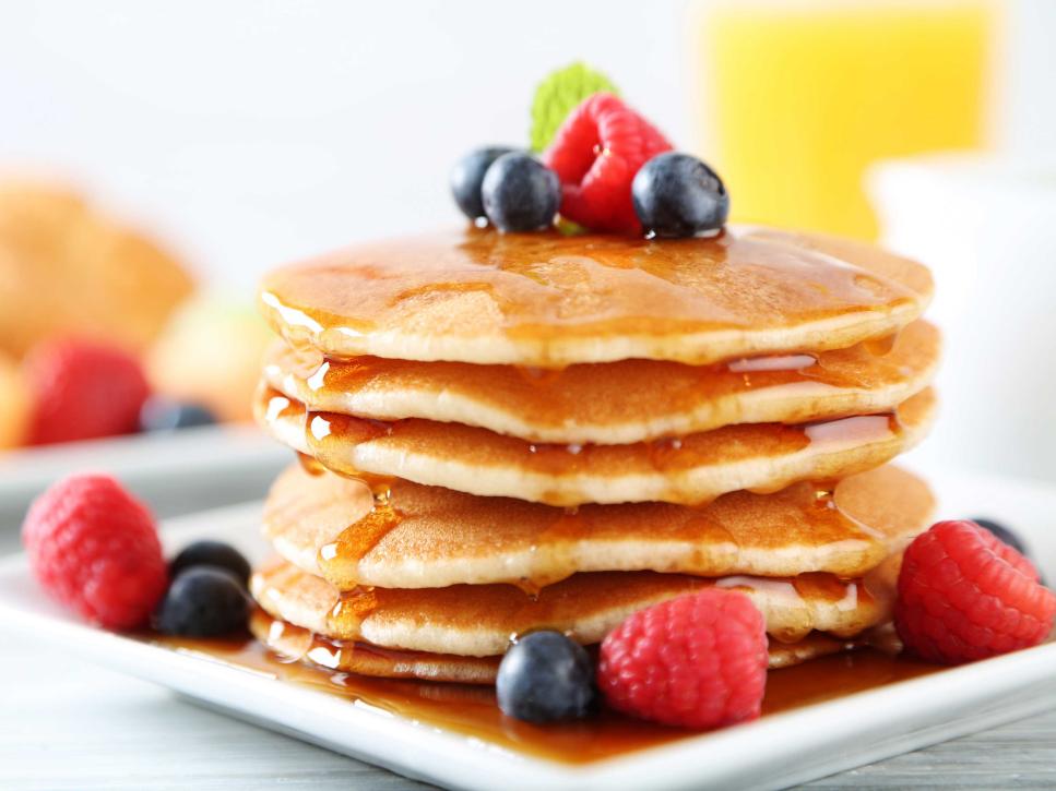 Stack of 6 pancakes with berries on top, covered with syup