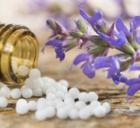 Homeopathic pellets being poured out of bottle, next to flowering plant